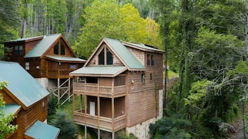 A cabin with a wooden exterior, a balcony, and a metal roof, surrounded by dense forest.