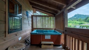 Une cabane en bois avec un jacuzzi sur la véranda, une petite table et un panneau d’avertissement indiquant la température de l’eau du jacuzzi.