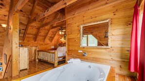A wooden cabin interior with a large wooden ceiling, a bedroom with a bed and a window, and a bathroom with a bathtub.