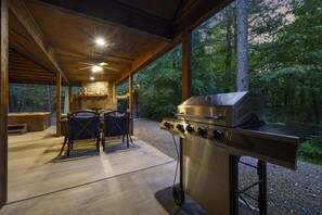 An outdoor covered patio with a gas grill, stone fireplace, and seating area. - LA ROCA - Luxury Cabin for Couples | Hot Tub, Outdoor Fireplace, Walk to Dining! (Broken)