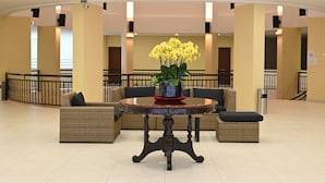A lobby with a round table, wicker furniture, and yellow flowers. - The Pines (Raub)