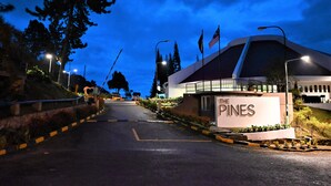 A hotel entrance with a sign reading "The Pines," a curved building, and a road leading up to it. - The Pines (Raub)