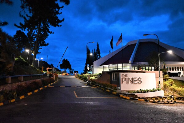 Entrada de un hotel con un letrero que dice "The Pines", un edificio con forma curva y una carretera que lo lleva.