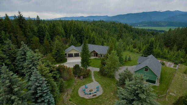 A house surrounded by dense forest with a clear view of mountains in the background. - Quail Cottage:  View Property - A Peaceful Place to Get Away (Bonners Ferry)