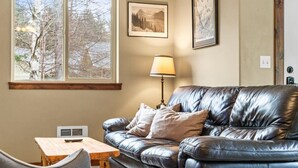 A room with a leather sofa, a small table, a lamp, and framed pictures on the wall. - Quail Cottage:  View Property - A Peaceful Place to Get Away (Bonners Ferry)