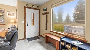 A cozy entryway with a white door, a bench, a small table with books, and a window with a view of trees. - Quail Cottage:  View Property - A Peaceful Place to Get Away (Bonners Ferry)