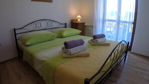 A neatly made bed with green and yellow bedding, a bedside lamp, and a window with sheer curtains. - Antique Apartment With Balcony (Stari Grad)