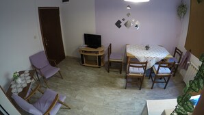 A room with a dining table, chairs, a television on a stand, a door, and a ceiling light. - Antique Apartment With Balcony (Stari Grad)