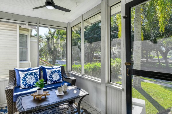 A covered porch with a seating area, a ceiling fan, and large windows offering a view of the outdoors.