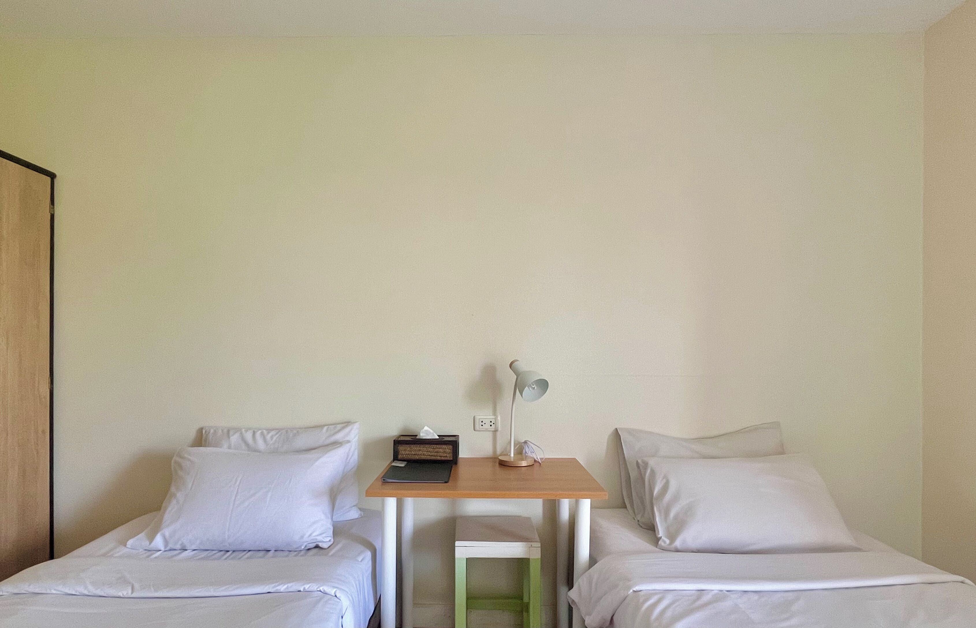 A room with two single beds, a small wooden table with a lamp, and a bedside table with a radio.
