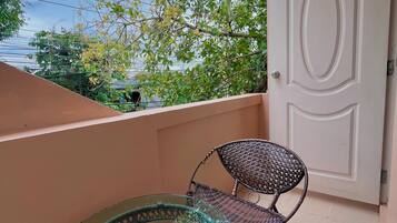 A glass-top table with a wicker chair on a balcony with a door and power lines in the background.