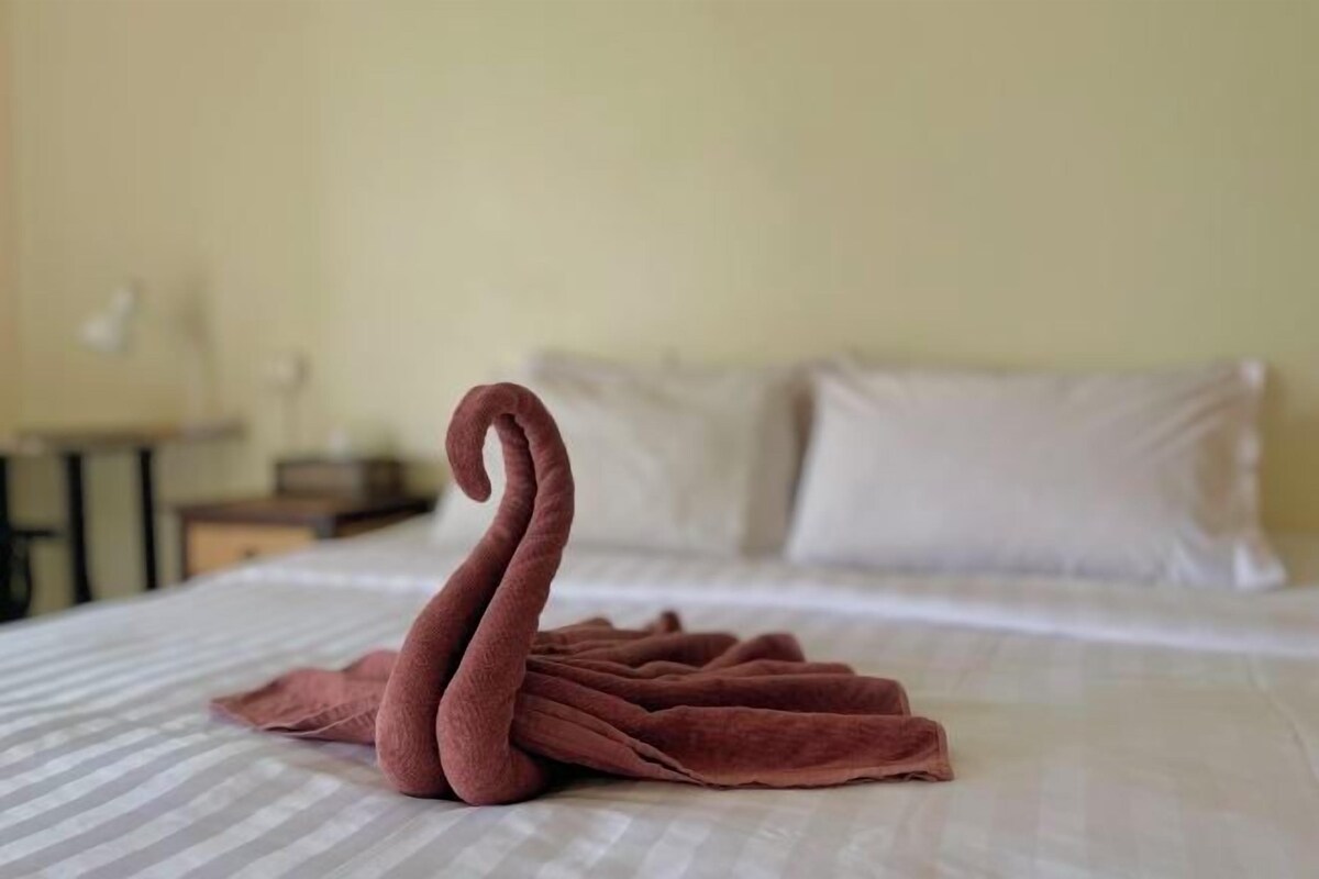 A neatly made swan-shaped towel on a bed with a striped bedspread and white pillows.