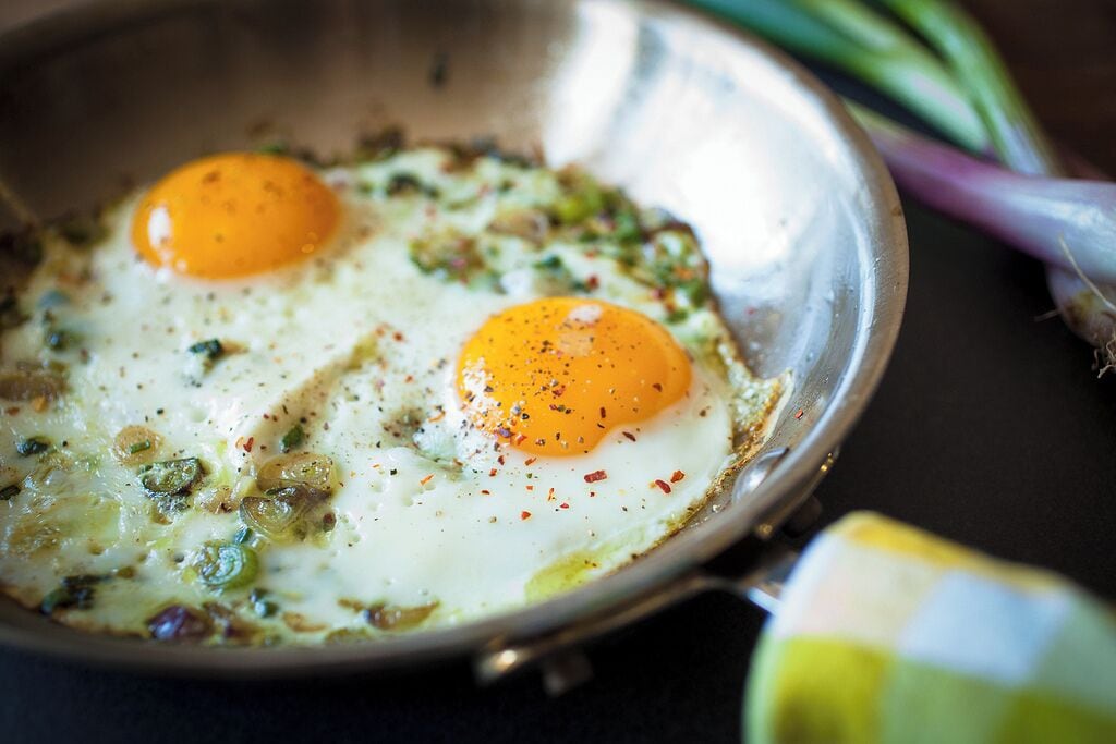 A frying pan with two sunny-side-up eggs and green onions.