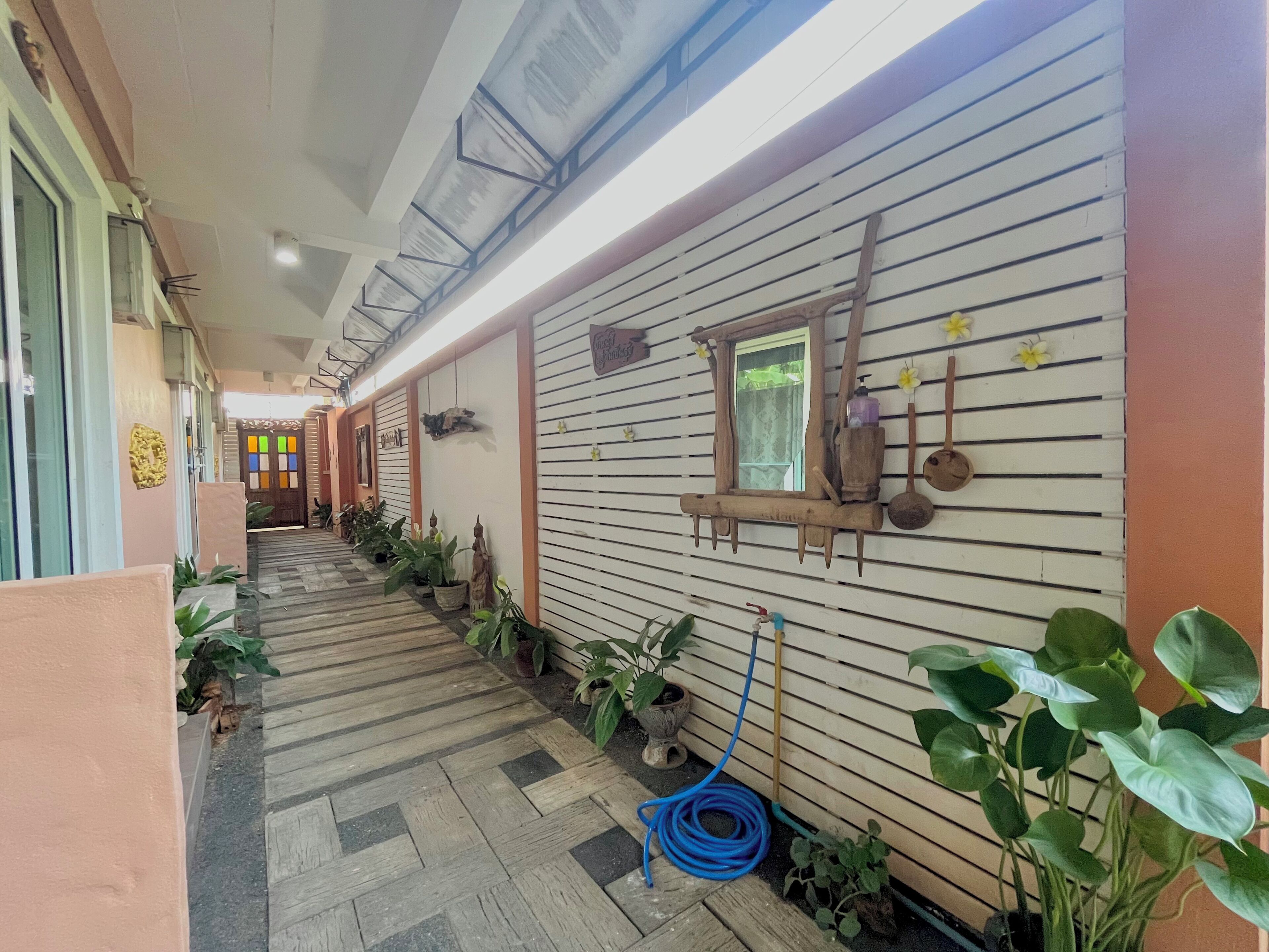 A hallway with a wooden floor, potted plants, and a blue garden hose.