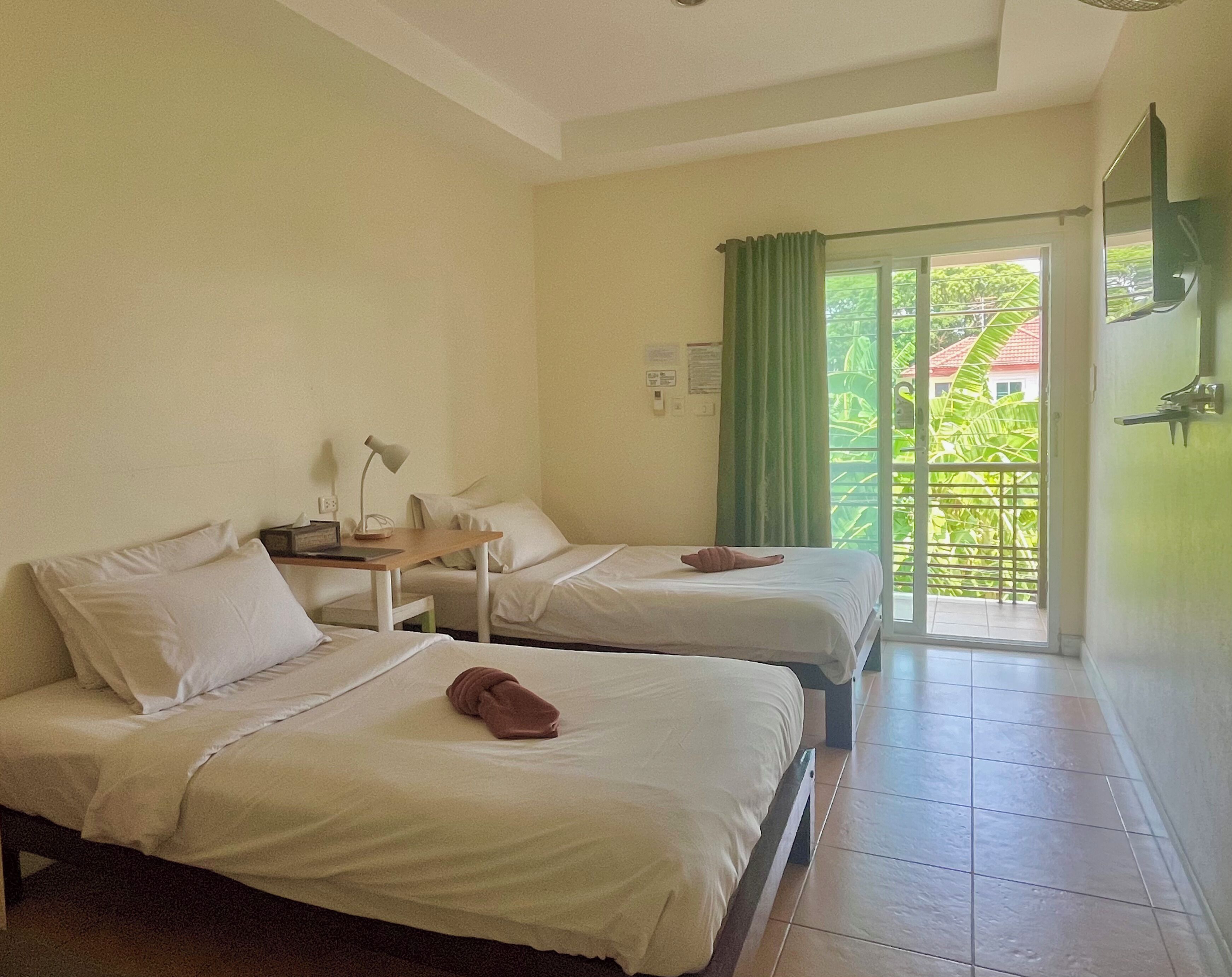 Une chambre d’hôtel avec deux lits, un bureau, une lampe et une vue sur la verdure, accessible par une porte coulissante.