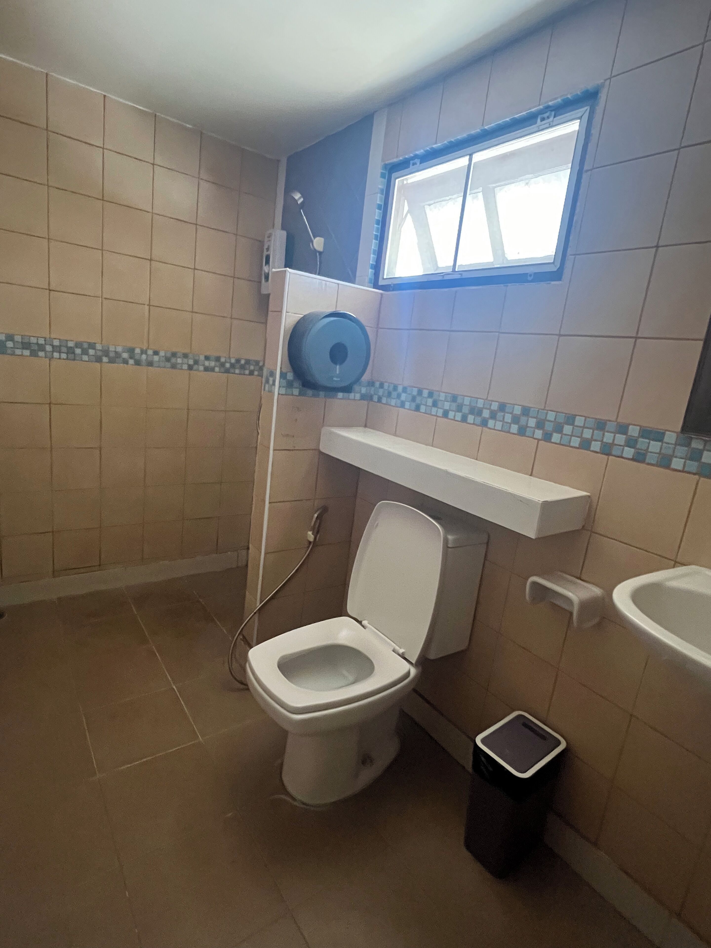 Ein Badezimmer mit Toilette, Handtrockner, Fenster und Mülleimer.