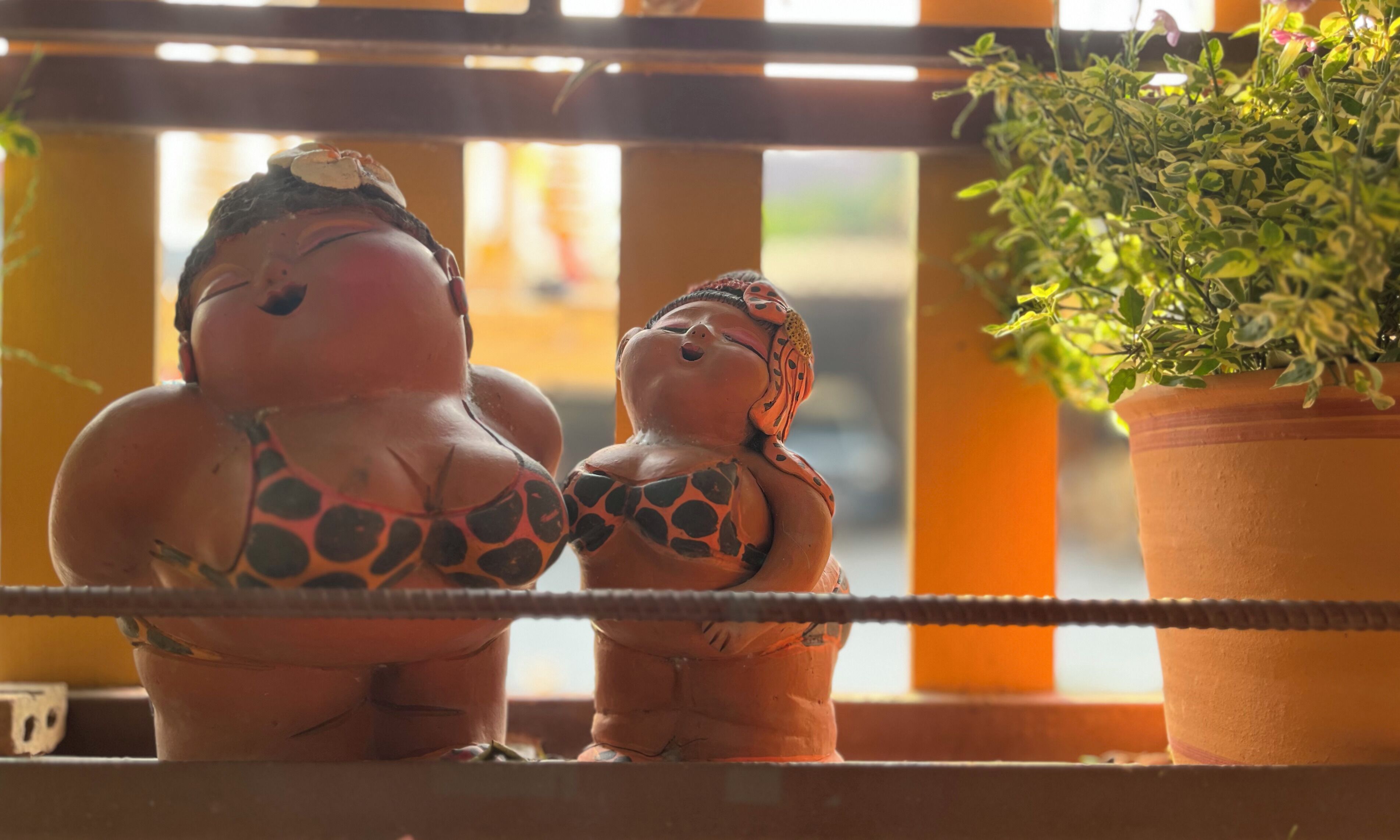 Zwei Keramikfiguren auf einer Balustrade, eine größer, eine kleiner, mit einem Blumentopf daneben.