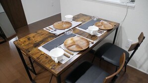 A dining table with wooden chairs, white plates, and cutlery. - Nagayama Whole Apartment (Asahikawa)