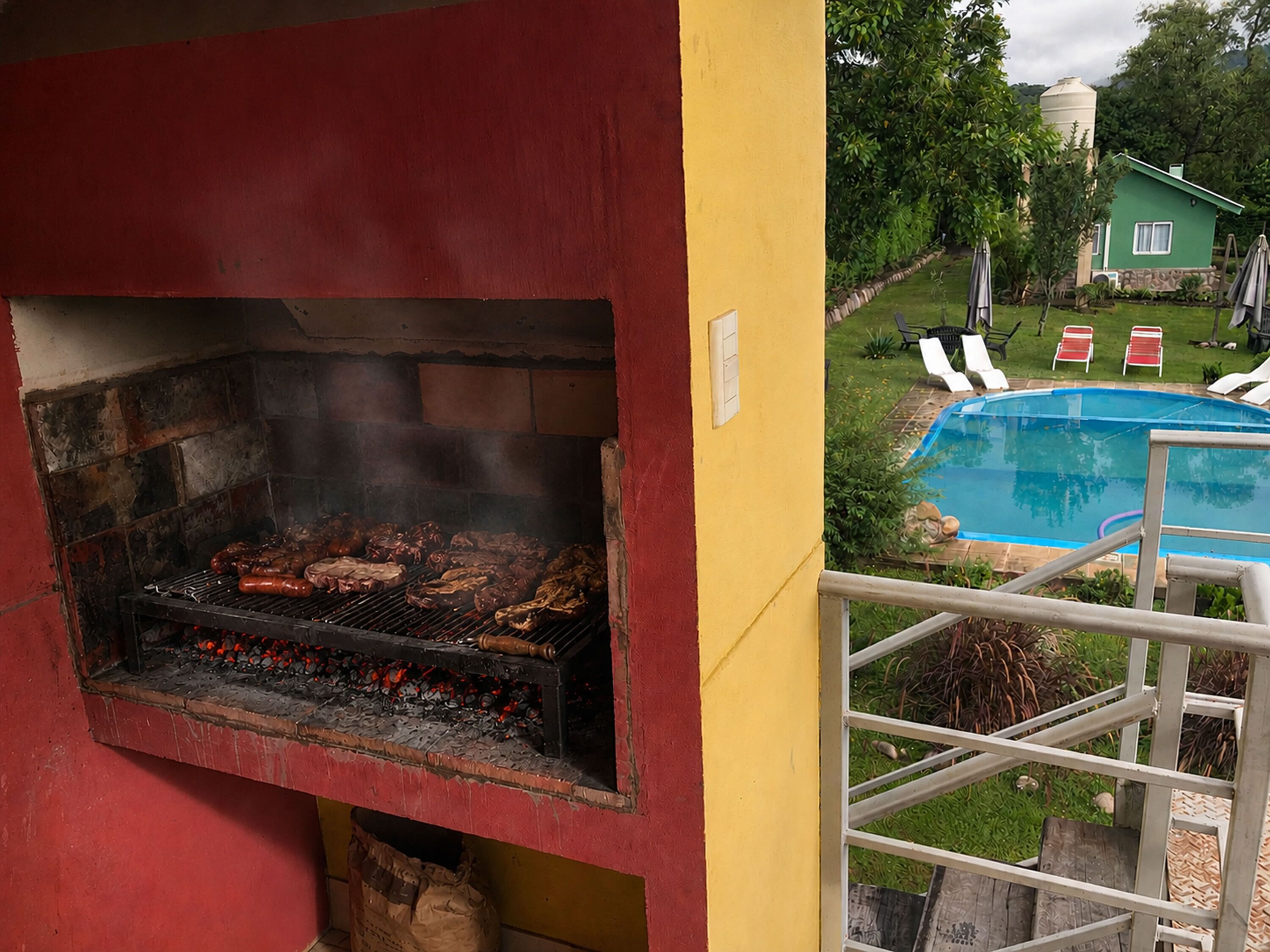 Uma churrasqueira, uma piscina e uma casa ao fundo.