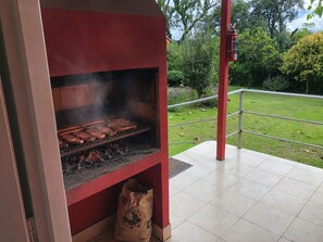 Un barbecue avec de la nourriture en train de cuire, un extincteur et un espace extérieur recouvert d’herbe.