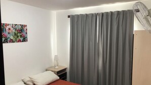 Et hotelværelse med en seng, et natbord med lampe, en stor grå gardin og en ventilator.