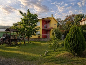 A multi-story building with a balcony, surrounded by a well-maintained lawn and trees.