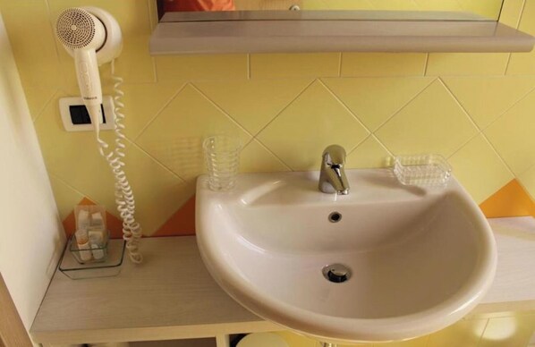Ein Badezimmer mit einem weißen Waschbecken, einem Spiegel und einem Fön auf einem an der Wand befestigten Regal.