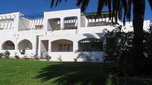 A white building with multiple arched windows and balconies, surrounded by a well-maintained lawn and palm trees. - Impressive in Ground Floor With Terrace of 2 Rooms and Pool (Vera)
