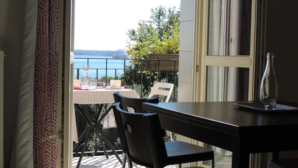 Un balcon ouvert avec une table et des chaises, offrant une vue panoramique sur la mer et la verdure.