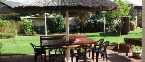 An outdoor patio with a thatched umbrella, a wooden table, and chairs.
