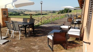 An outdoor patio with a table and chairs, a view of the countryside, and a fence.