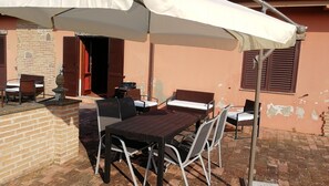 Un patio al aire libre con una mesa, sillas, un muro de ladrillo y una sombrilla blanca que da sombra.