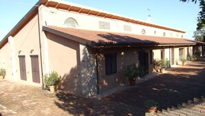 A building with a tiled roof, brick walls, and multiple windows. There are potted plants along the pathway and a metal fence in the foreground.