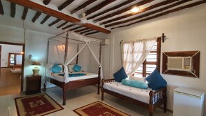 A bedroom with a four-poster bed, a bedside table with a lamp, a small bedside table with a lamp, a wooden wardrobe, and a white air conditioning unit. - Mbv Hotel Annex Family Rooms (Matemwe)