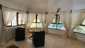 A room with large windows, white curtains, a small round table, and two black chairs. - Mbv Hotel Annex Family Rooms (Matemwe)