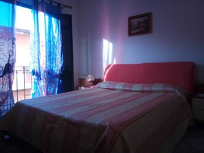A bedroom with a bed, a nightstand, a lamp, and a window with curtains.