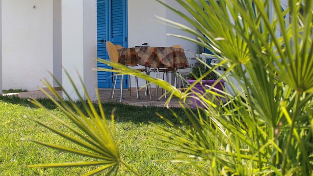 A patio with a table and chairs, a blue door, and a white wall. - S'olivariu Village Guest House Swimming Pools Heart Of Sulcis (Piscinas)