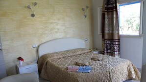 A bedroom with a bed, bedside tables, a nightstand, a chair, and a window with curtains. - S'olivariu Village Guest House Swimming Pools Heart Of Sulcis (Piscinas)