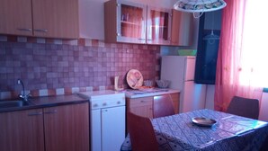 A compact kitchen with wooden cabinets, a tiled backsplash, a stove, a sink, and a dining table with chairs. - S'olivariu Village Guest House Swimming Pools Heart Of Sulcis (Piscinas)