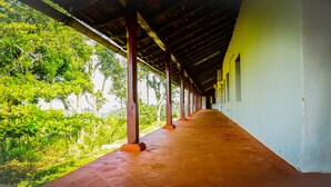 A covered corridor with a tiled floor, supported by wooden pillars, leading to a building with white walls and a yellow exterior. - Deluxe Double Room In British Bungalow (Vythiri)