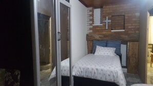 A bedroom with a bed, a wooden headboard, a brick wall, and a cross decoration. - Room in House - Patzerella's Cozy Nest (Krugersdorp)