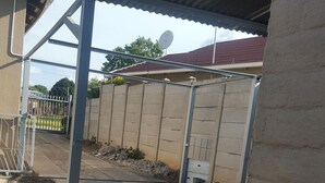 A covered outdoor area with a metal roof, a concrete wall, and a metal gate. - Room in House - Patzerella's Cozy Nest (Krugersdorp)