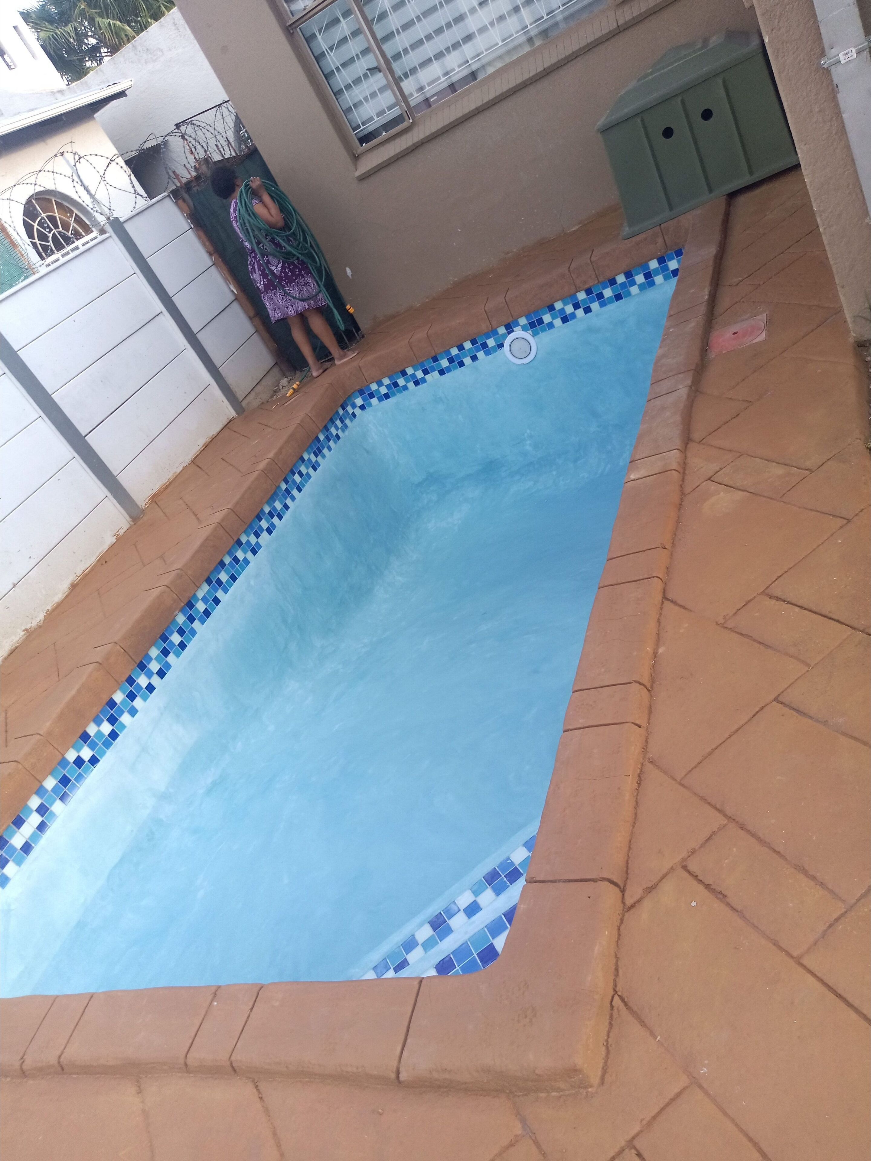 Piscina retangular com bordas azulejadas em azul e branco, rodeada por um pátio de tijolos.