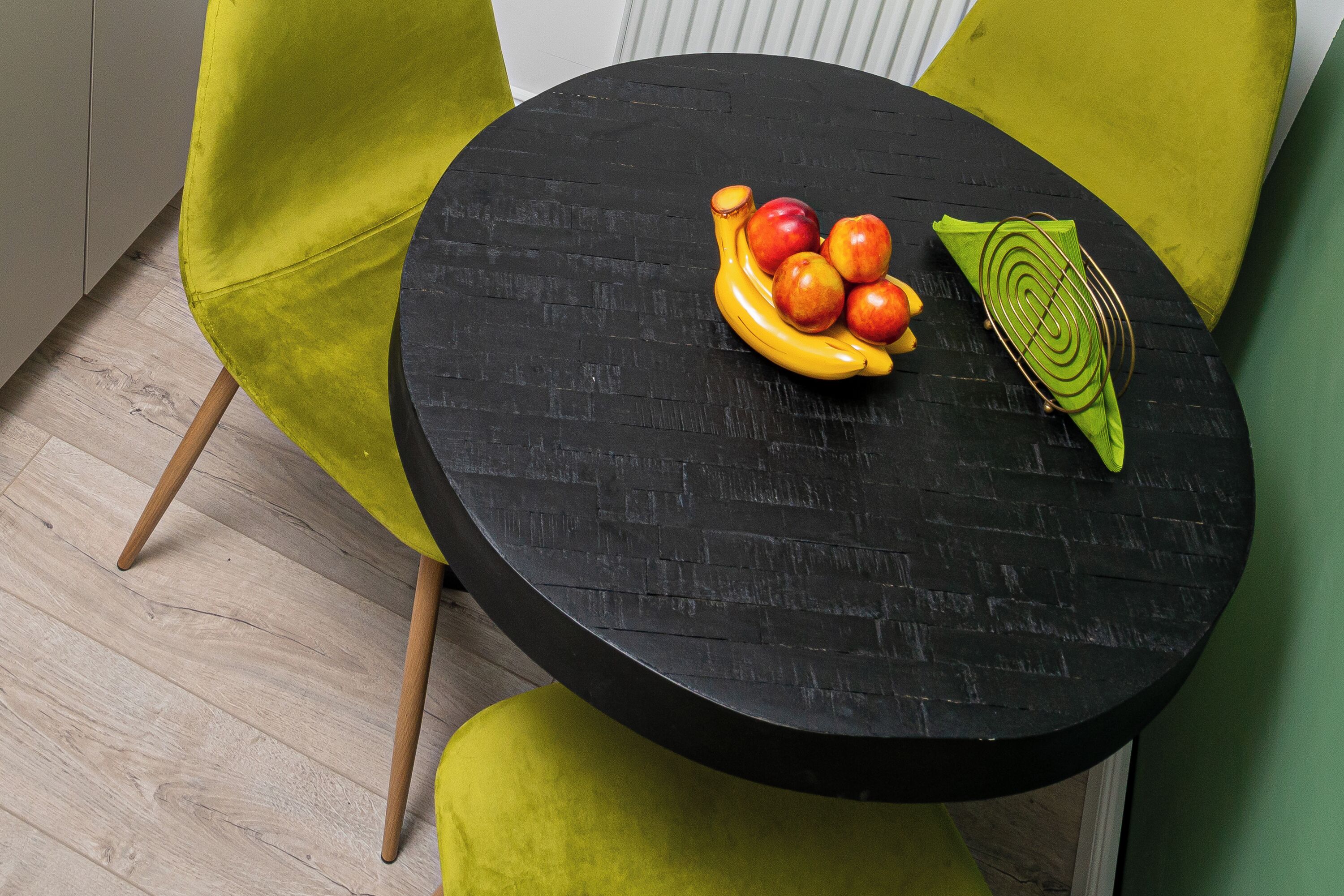 Una mesa redonda negra con textura de ladrillo, rodeada por una silla verde con patas de madera.