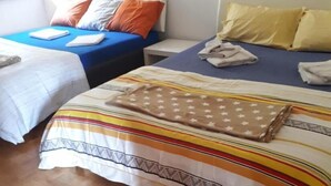 A hotel room with two beds, one with a striped bedspread and the other with a plain blue bedspread. - Appartamenti La Bettola Chez Patty (Castel San Pietro)