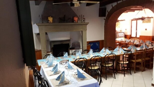 A dining area with tables set for a meal, a fireplace, and a view through an arched doorway. - Appartamenti La Bettola Chez Patty (Castel San Pietro)
