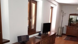 A living room with a wooden entertainment center, a flat-screen TV, a laptop, and a floor lamp. - Appartamenti La Bettola Chez Patty (Castel San Pietro)