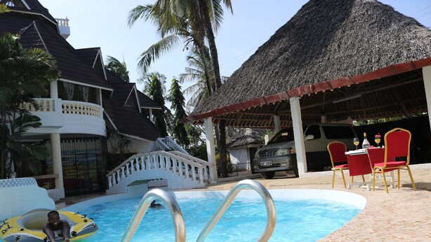 A swimming pool with a thatched-roof structure, a covered seating area, and a poolside chair.