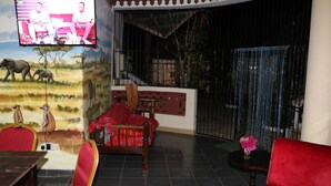 A room with a television mounted on the wall, a dining area with chairs and a table, and a large window with a view of the outside.