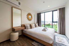 A modern hotel room with a large bed, a vanity with a mirror, a sunburst wall decoration, and a view of the city through large windows.